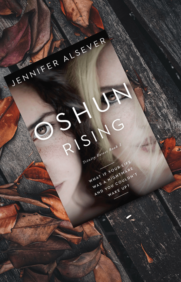 A paperback book titled 'Oshun Rising' by Jennifer Alsever is placed on a dark wooden surface surrounded by brown autumn leaves. The book cover features a split image of two women with different hair and skin tones, and a quote about nightmares and waking up.