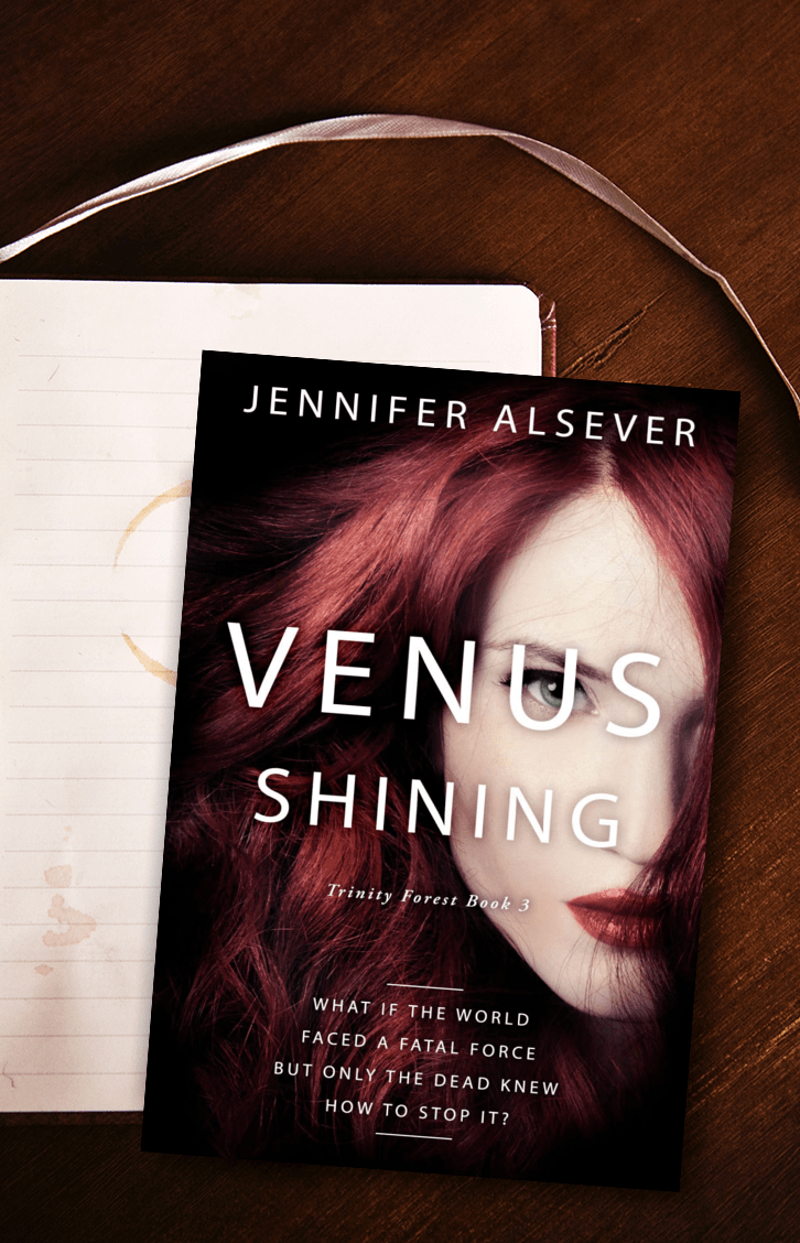 A book titled 'Venus Shining' by Jennifer Alsever, featuring a woman's face with red hair and red lipstick, lying on a wooden surface next to a lined notebook with a ribbon bookmark.