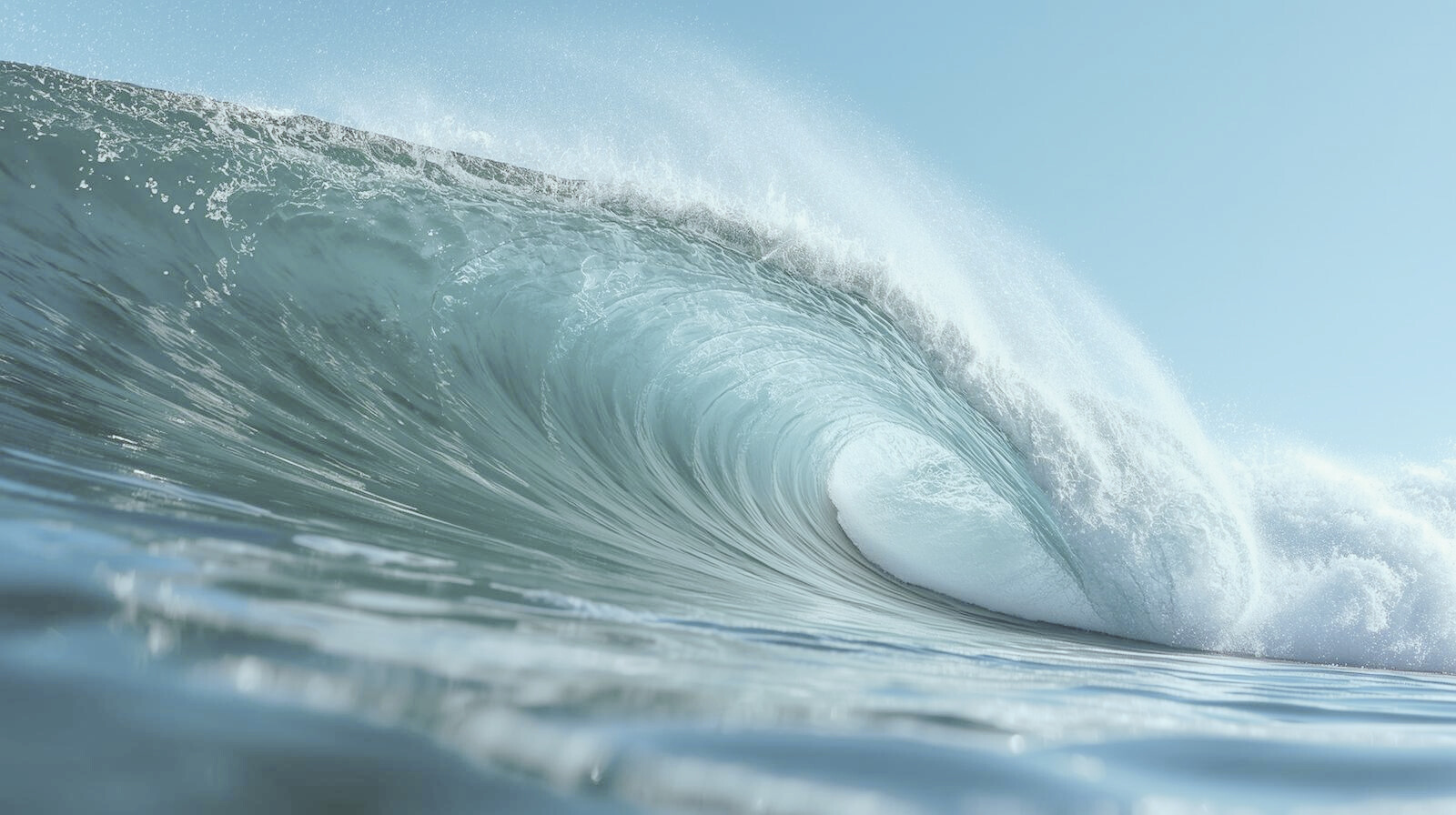 An ocean wave curling with white foam at the crest, viewed from the water surface with a clear sky background.