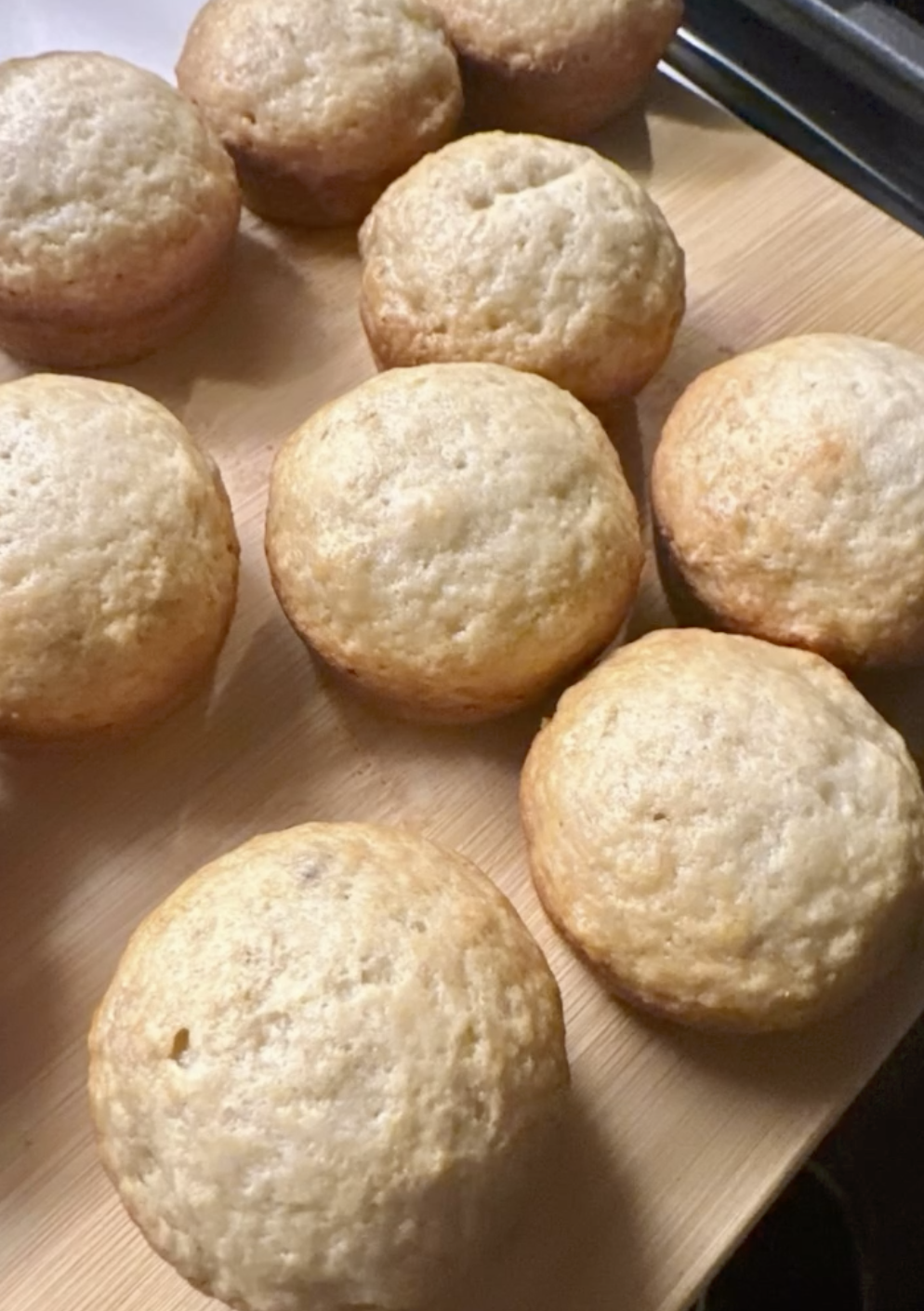 golden banana bread muffins cooling on a wooden cutting board
