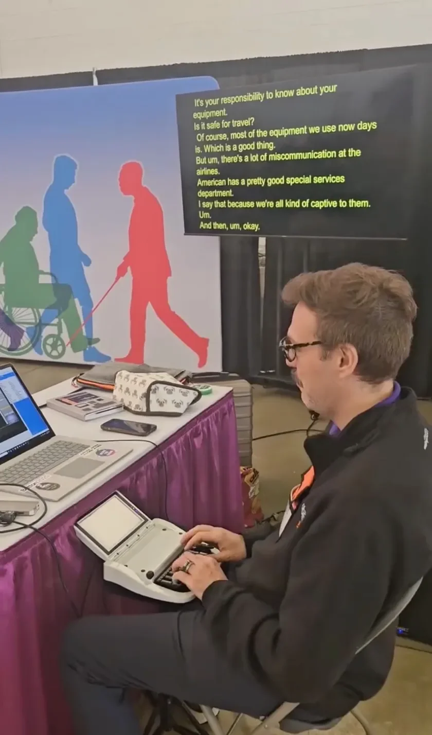 Thomas Herman operating a steno machine at a live event, with real-time captions displayed on a large screen behind him.