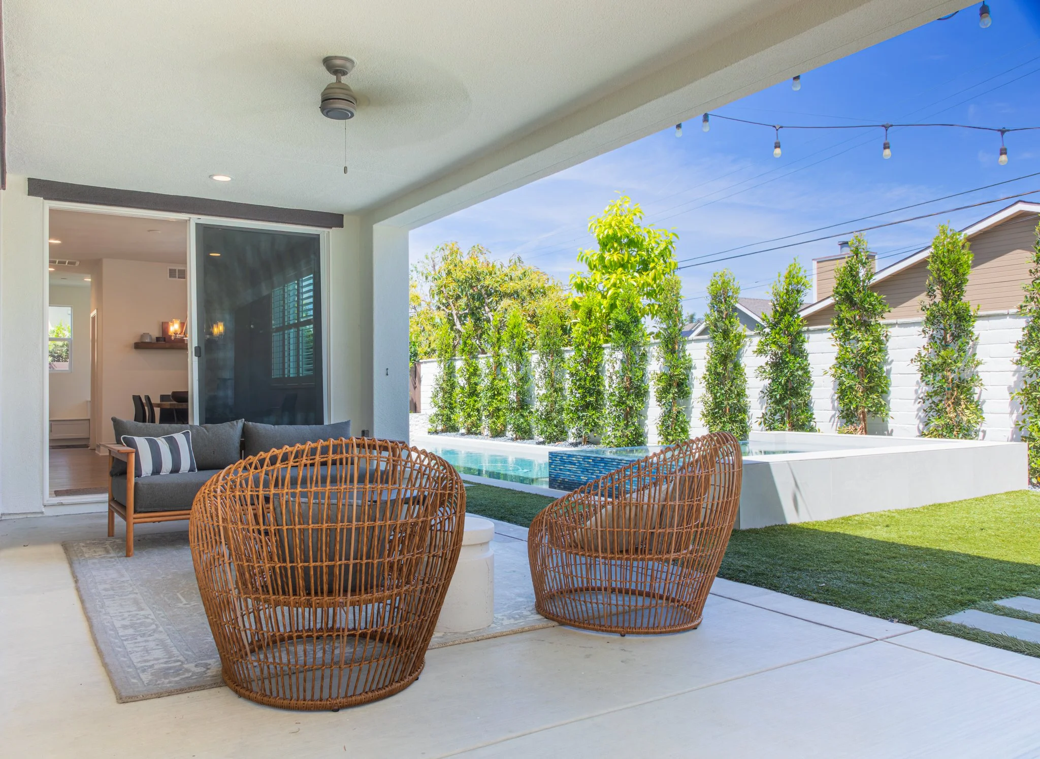 Outdoor patio with rattan chairs, a sofa, and a view of a backyard with trees and a small pool.
