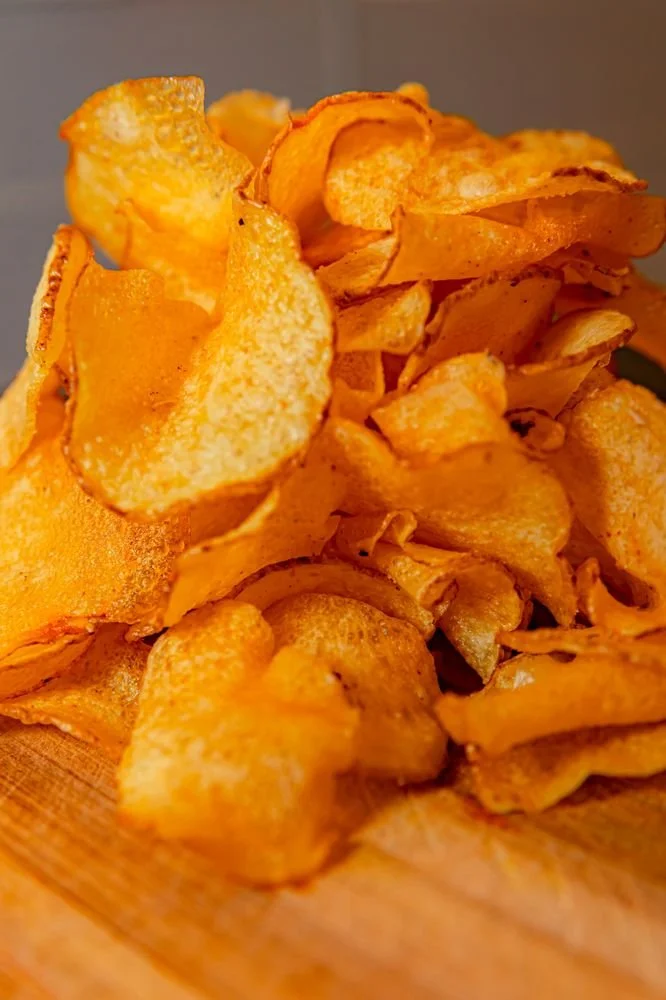 A close-up of a pile of potato chips on a wooden surface.