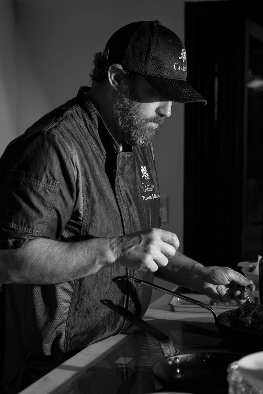 A man wearing a hat and apron, focusing on cooking in a kitchen.