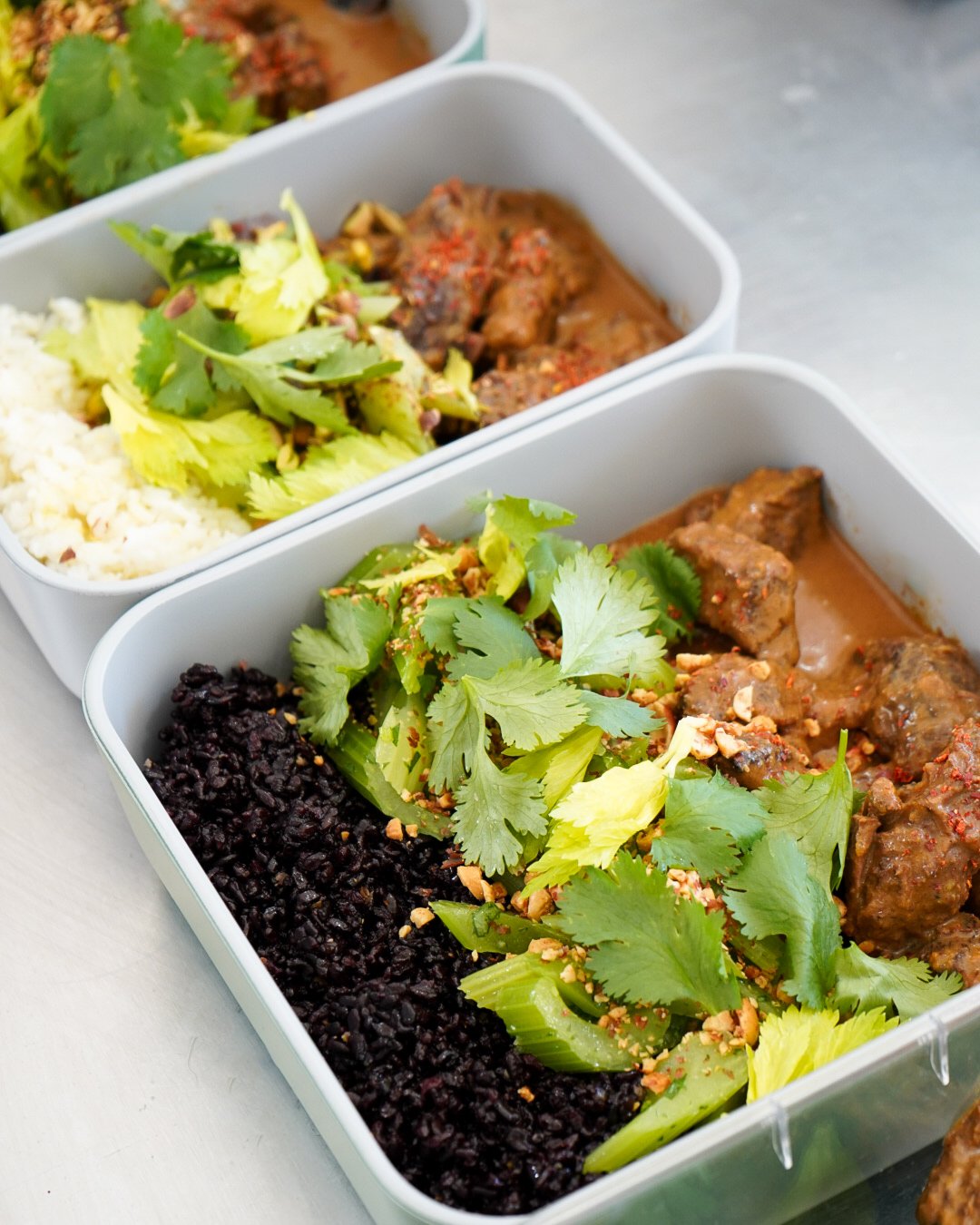 Meal prep containers with rice, black rice, beef stew, and salad with cilantro.