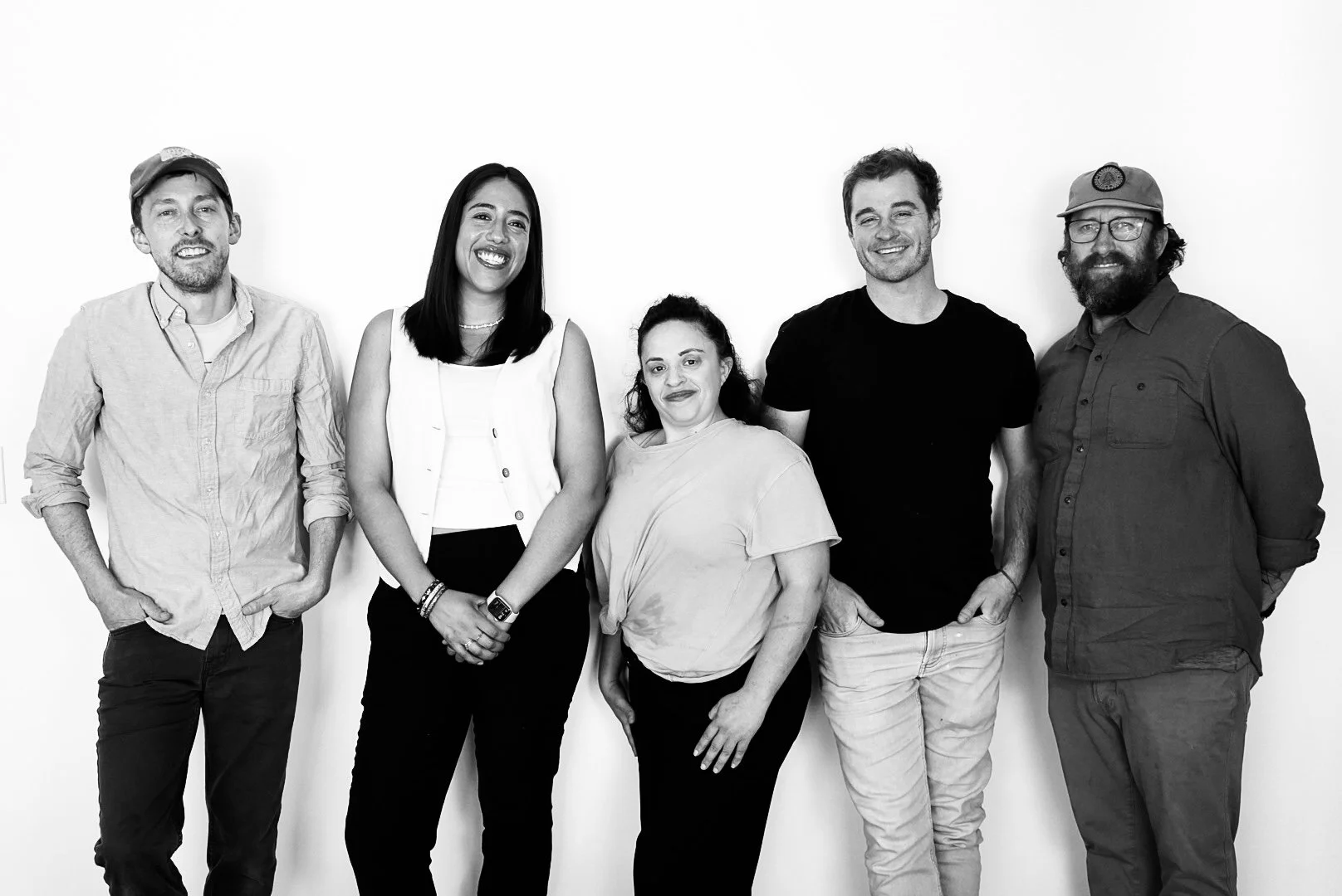 Group of five diverse people standing together against a plain background, smiling.