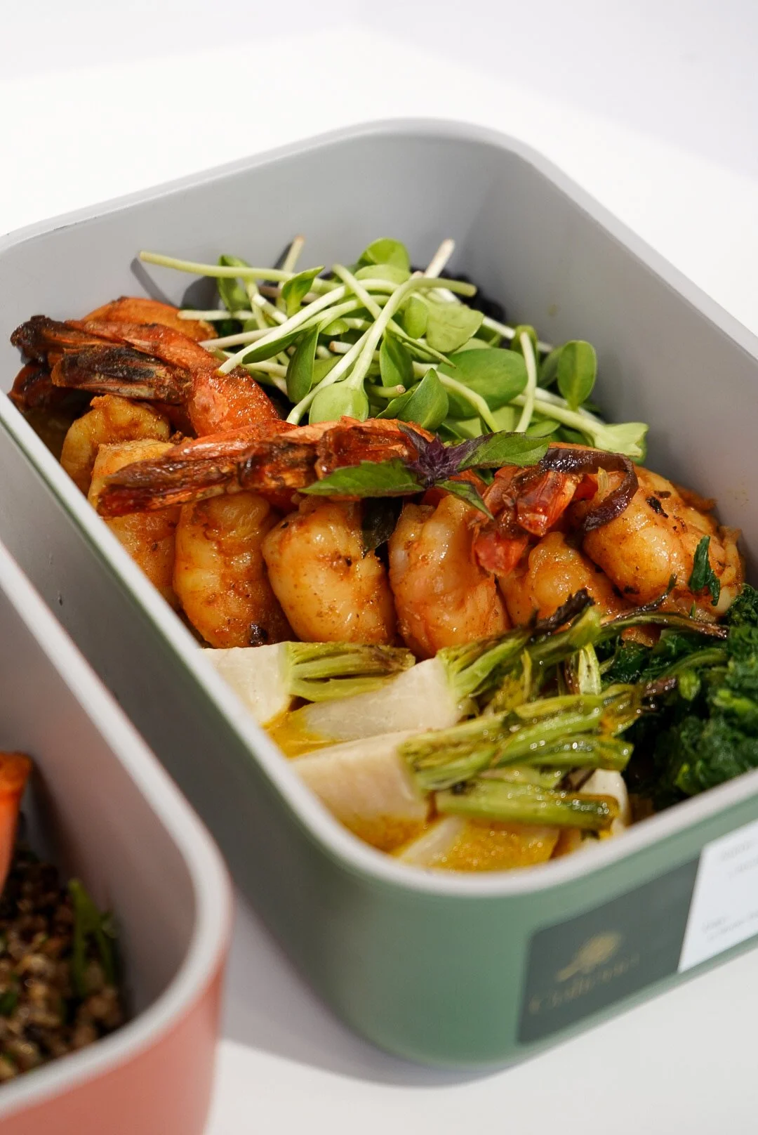 A dish with shrimp, greens, sprouts, and grilled meat inside a gray container.