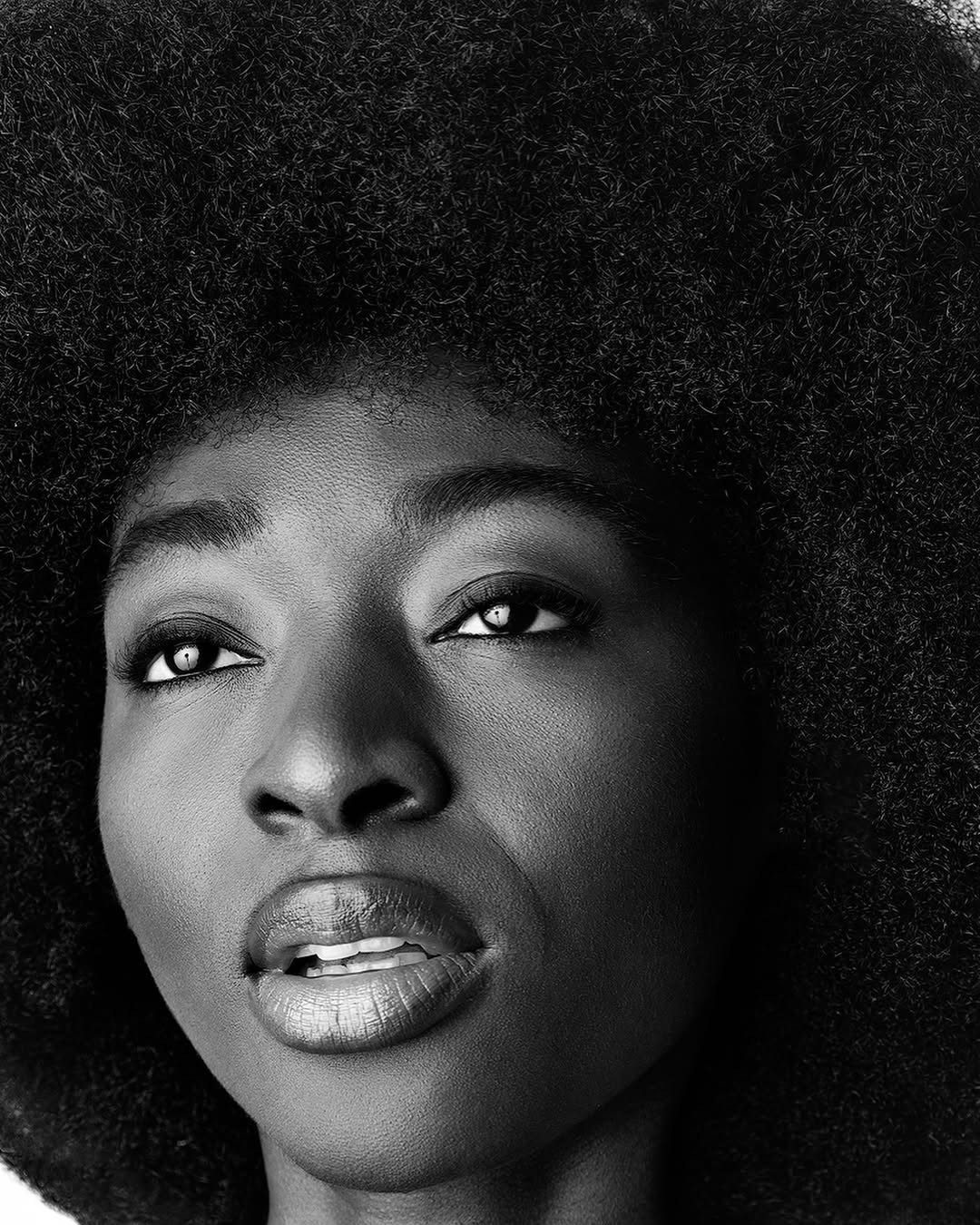 Close-up black and white portrait of a woman with natural hair, looking slightly upward.