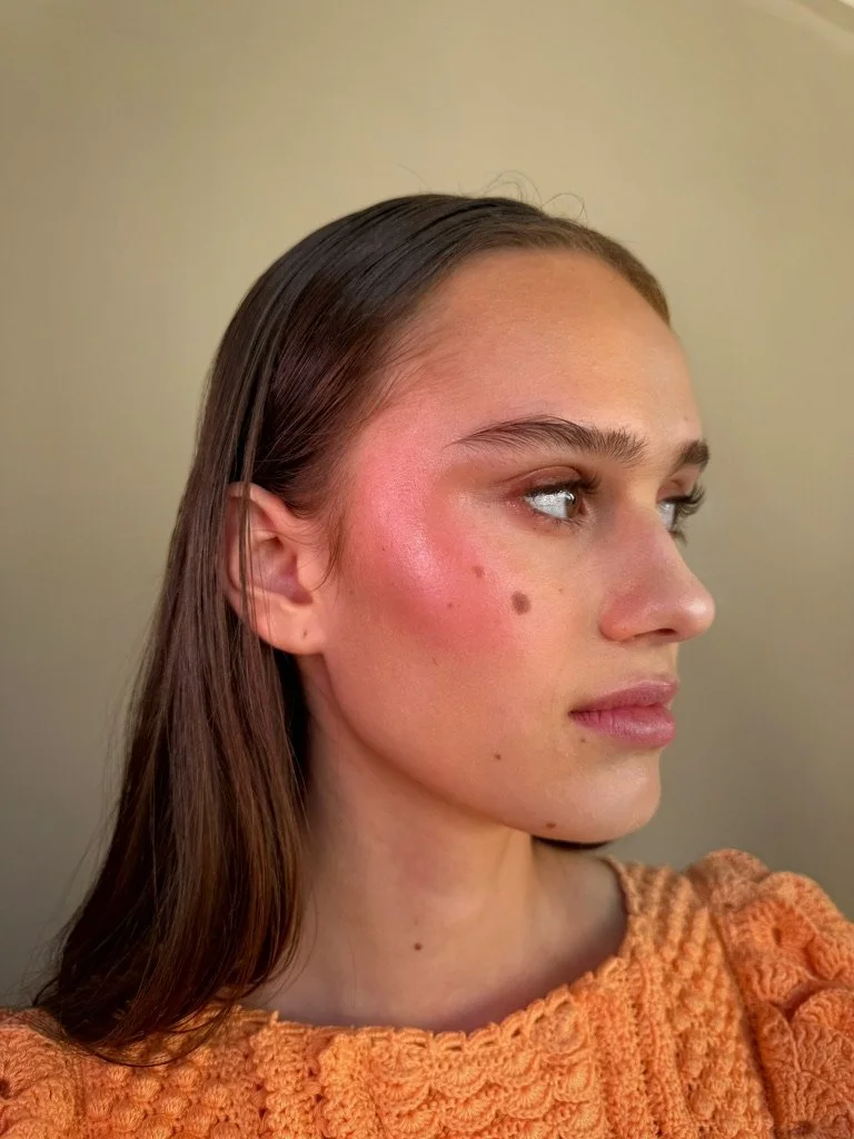 Side profile of a young woman with long brown hair, wearing an orange knitted sweater, looking to her right with a neutral expression.