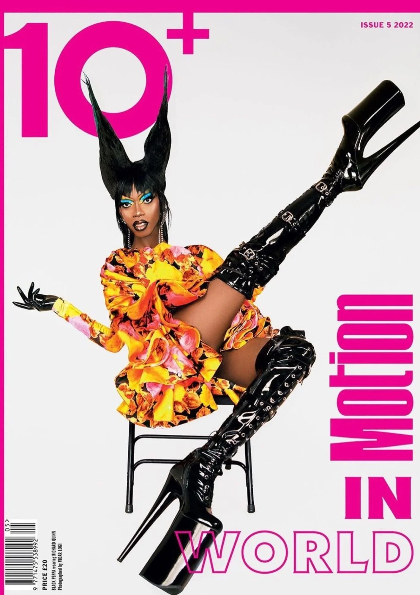 Fashion magazine cover featuring a woman with black hair styled upward, makeup with bright blue and yellow eyeshadow, wearing a colorful floral dress, black gloves, and thigh-high black shiny boots with high heels, sitting on a black chair against a 