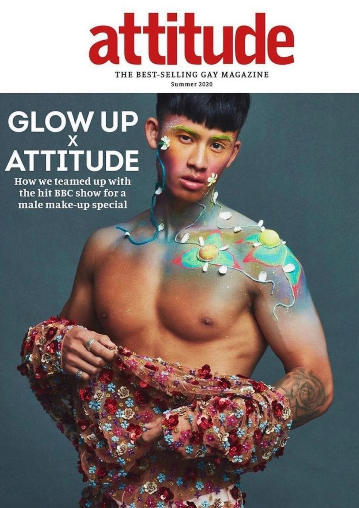 Magazine cover titled 'attitude' with a shirtless person with colorful makeup and floral accessories holding a floral fabric.