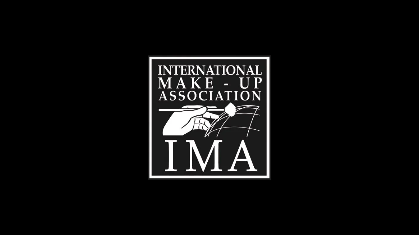 Logo for the International Make Up Association (IMA) featuring a hand holding a makeup brush above a stylized globe, with the organization's name.