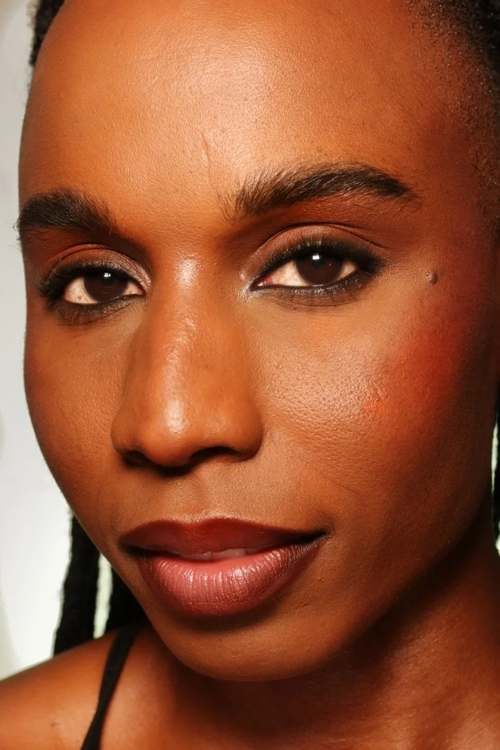 Close-up of a woman's face with makeup and dark hair styled in braids.