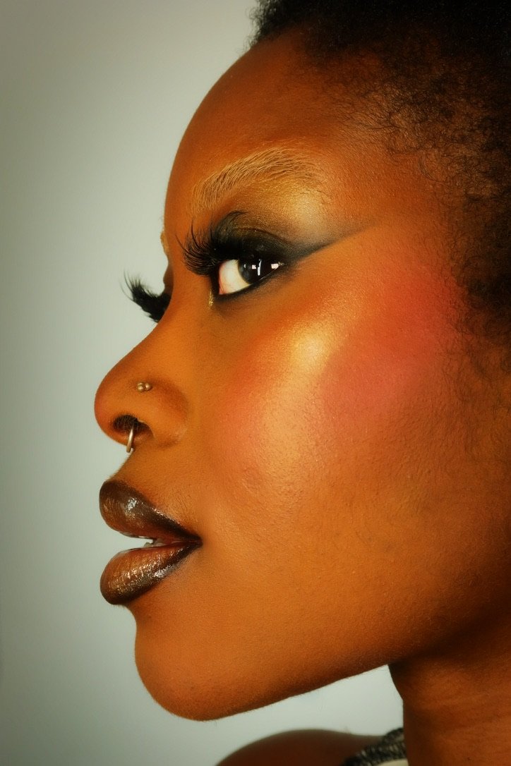 Profile of a woman with dramatic eye makeup, dark lipstick, and a nose piercing.
