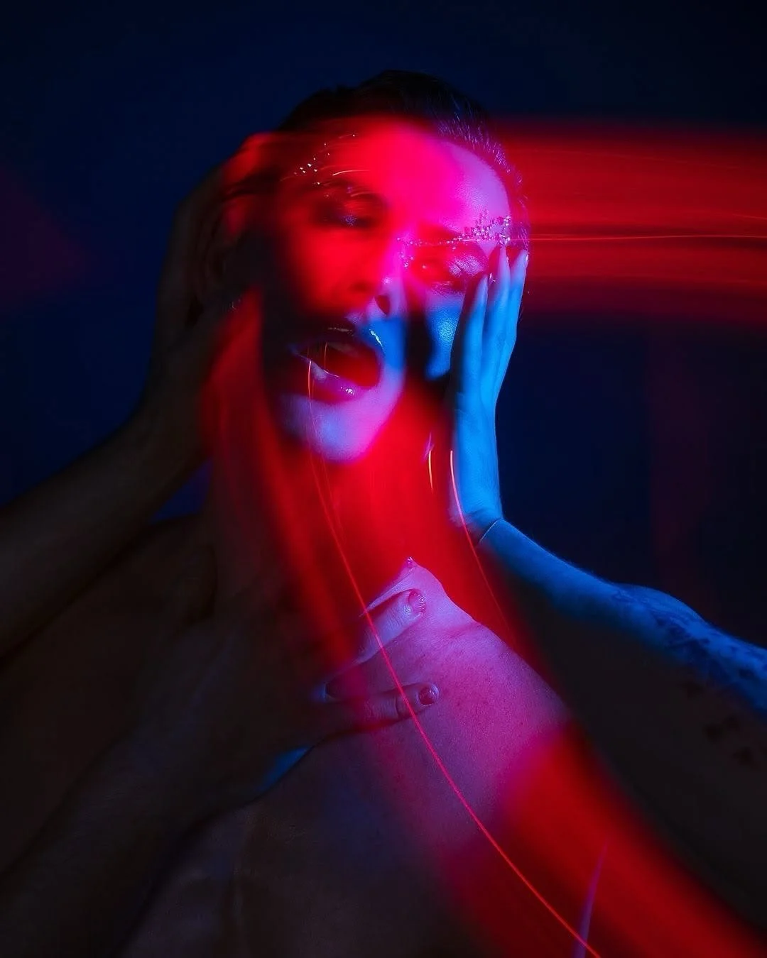 A woman with her hands on her face, illuminated by red and blue neon lights, creating a surreal and dramatic effect.