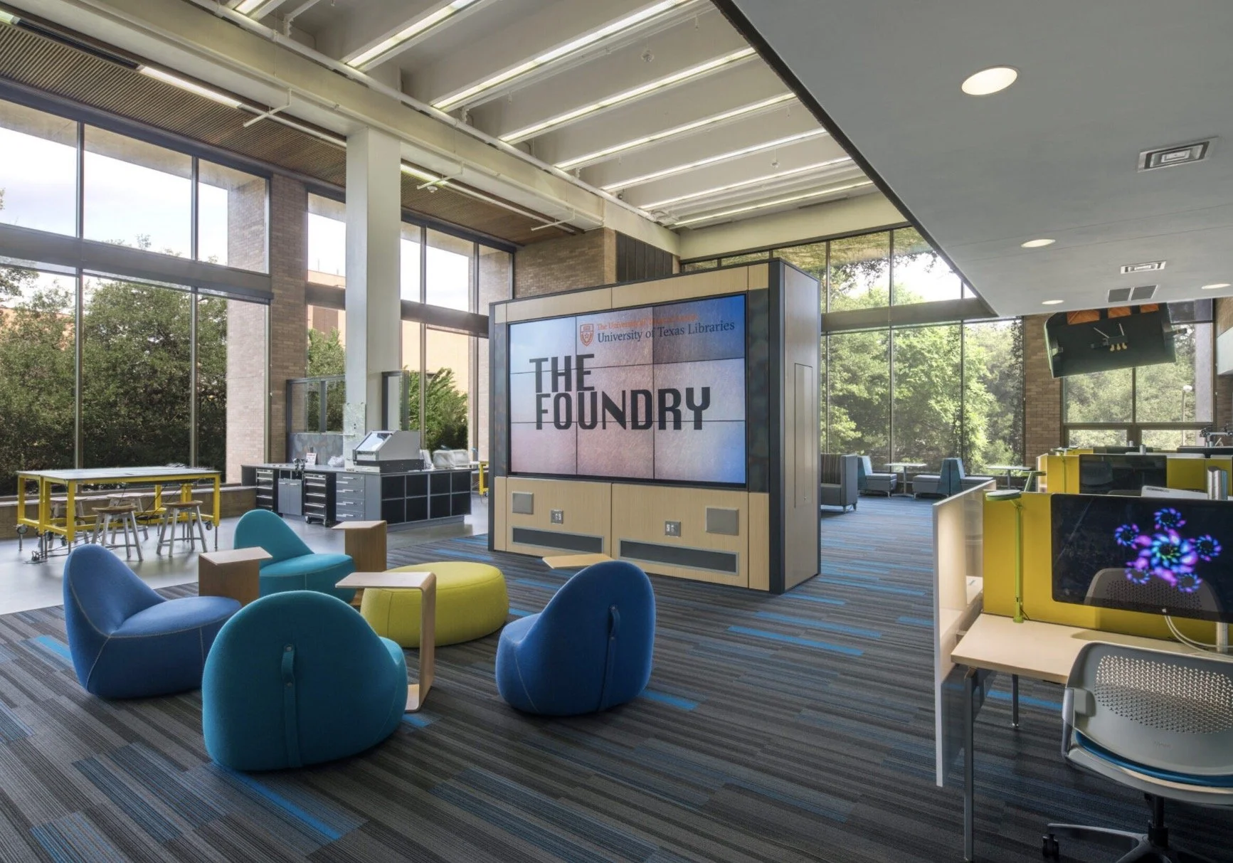 Modern library or study lounge with large windows, colorful seating, a large display screen reading 'The Foundry' with University of Texas Libraries logo, and various tables and tech stations.