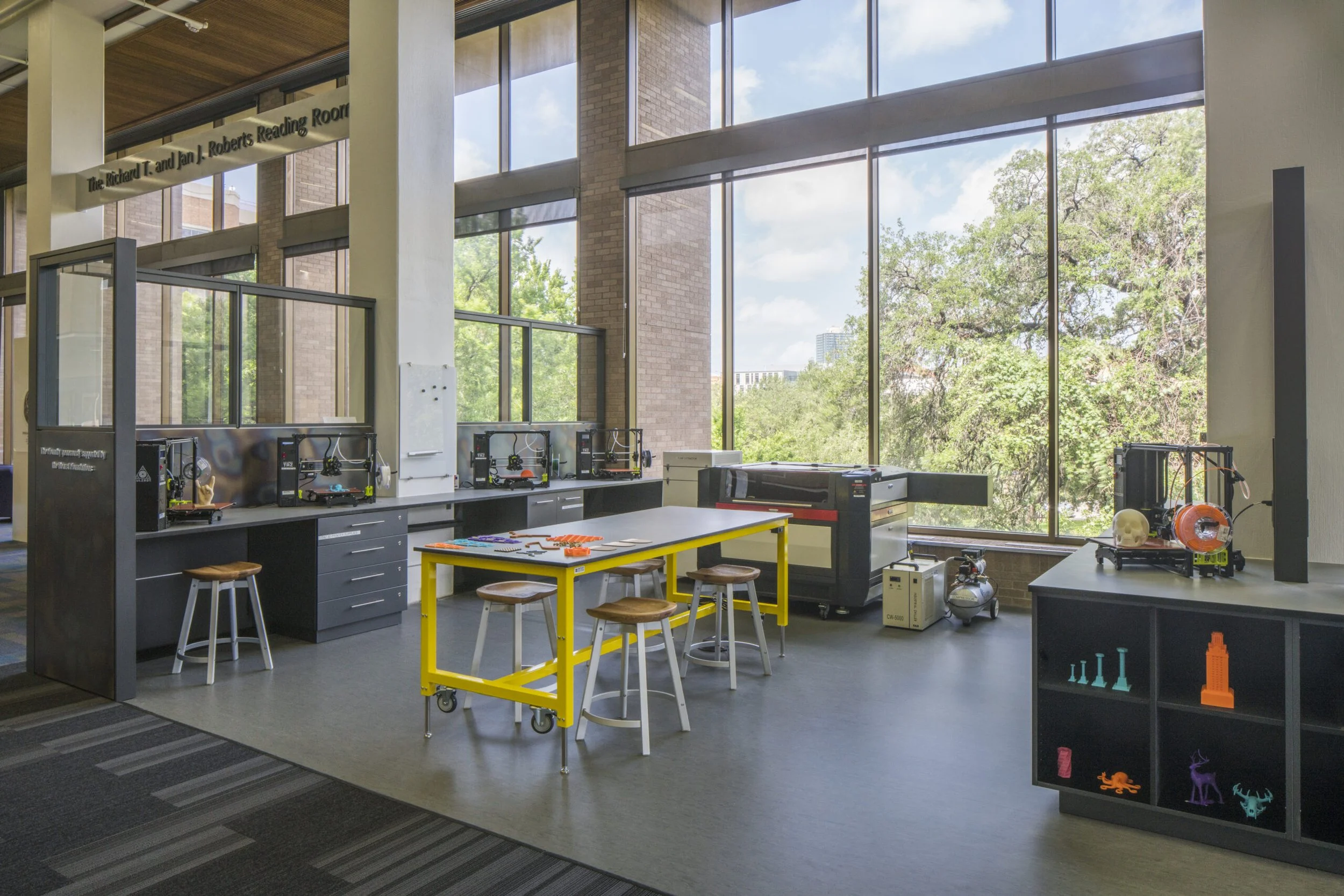 A makerspace classroom with large floor-to-ceiling windows, desks, and various scientific equipment and models for experiments.