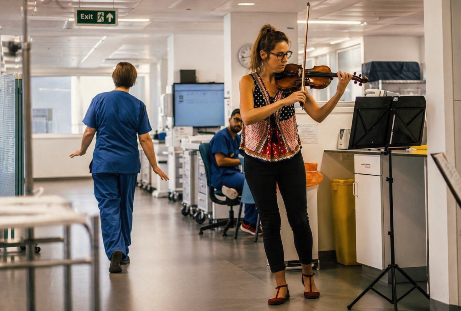 A woman playing the violin in a hospital corridor, with two nurses and medical equipment in the background.