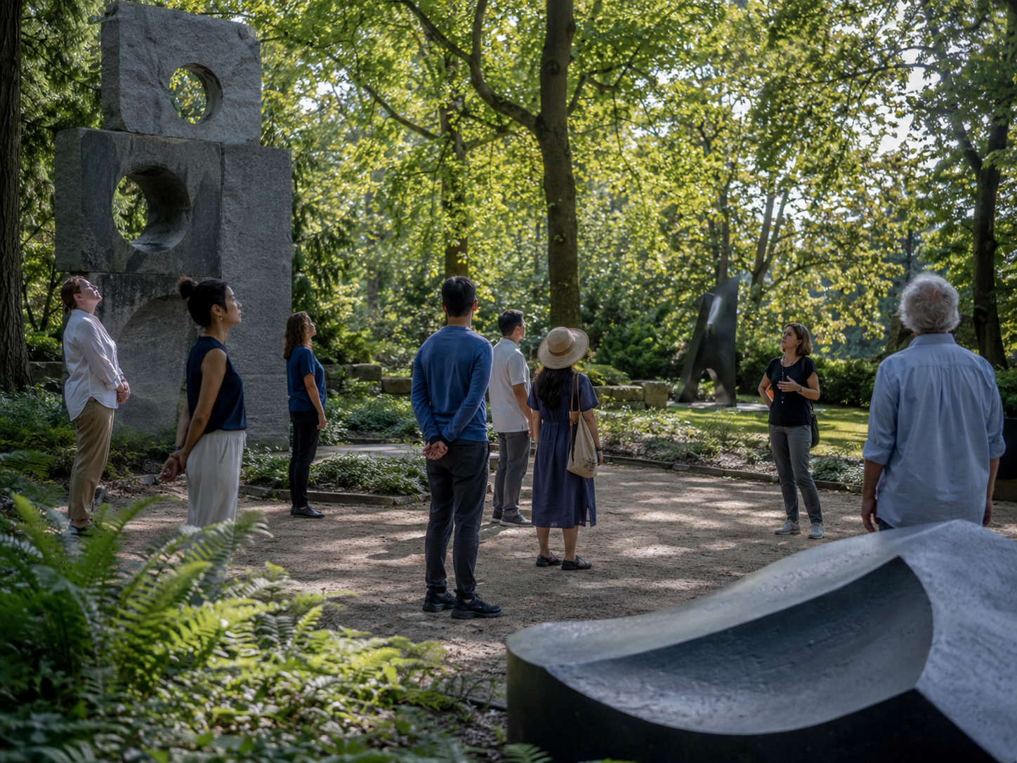 People standing in a circle listening to a tour guide in a lush green park with abstract sculptures and trees around as an example of Whole Health in Museums.