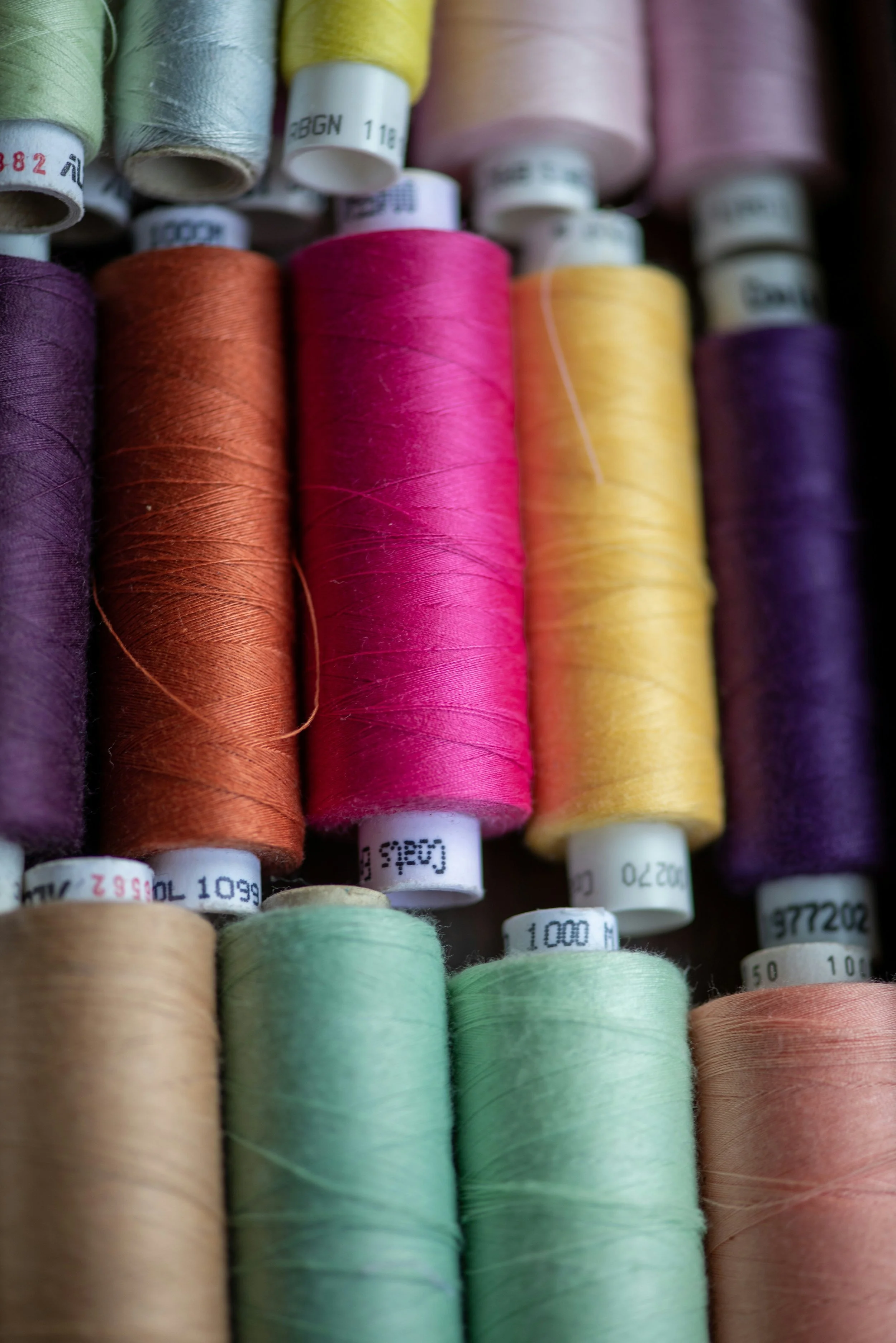Close-up of colorful sewing threads arranged vertically, showcasing various shades including purple, orange, pink, yellow, green, and beige.