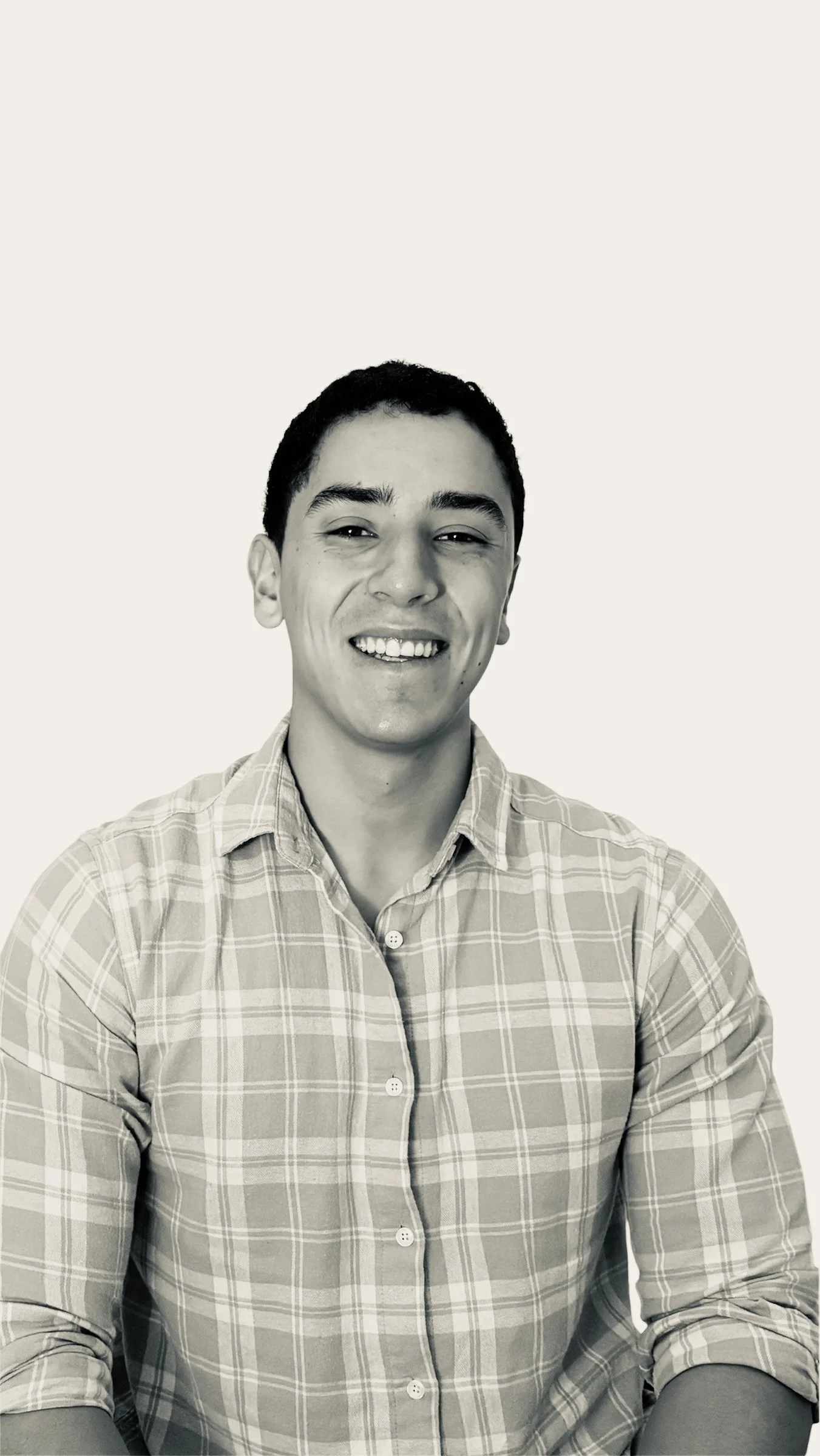 Retrato en blanco y negro de un joven sonriendo, usando una camisa de cuadros. Fondo claro.