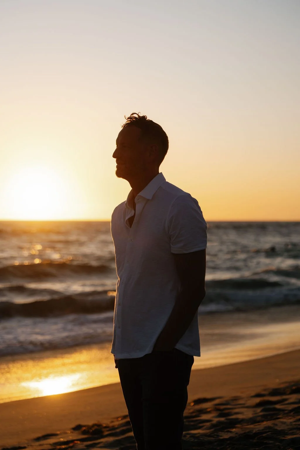 Silhouette of a man standing on the beach during sunset, with the ocean in the background.