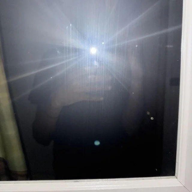 A person taking a photo of a bright flash of sunlight reflecting off a window, creating starburst effects.