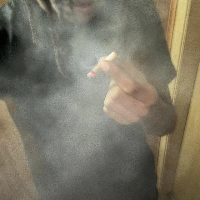 Person holding a lit cigarette in a cloudy, smoky environment.