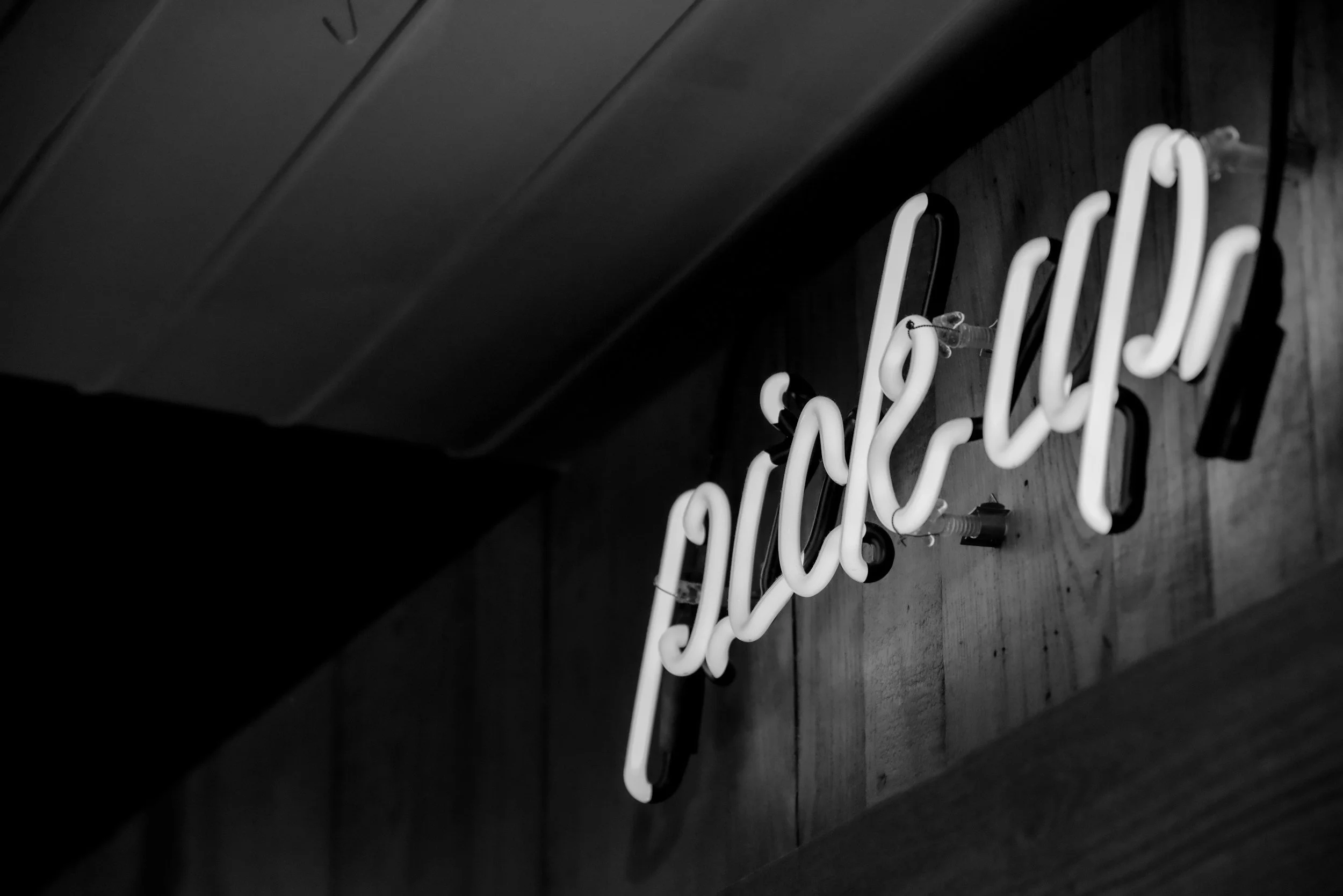 Neon sign that reads 'Pick Up' hanging on a black wall.