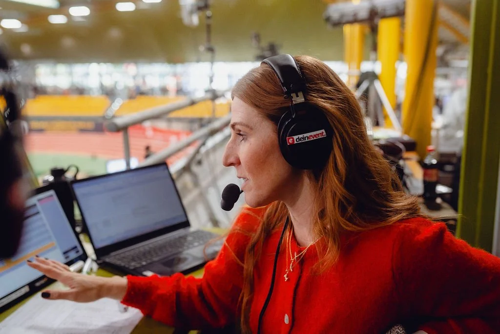 Alexandra Dersch, Moderatorin, Kommentatorin, ZDF, Leichtathletik, Curling, Para Ski Alpin, Skispringen, Sportstudio, TV-Kommentar, Livestream, Frau mit roten Haaren im Podcast-Studio, trägt Kopfhörer mit Mikrofon, arbeitet an mehreren Laptops.