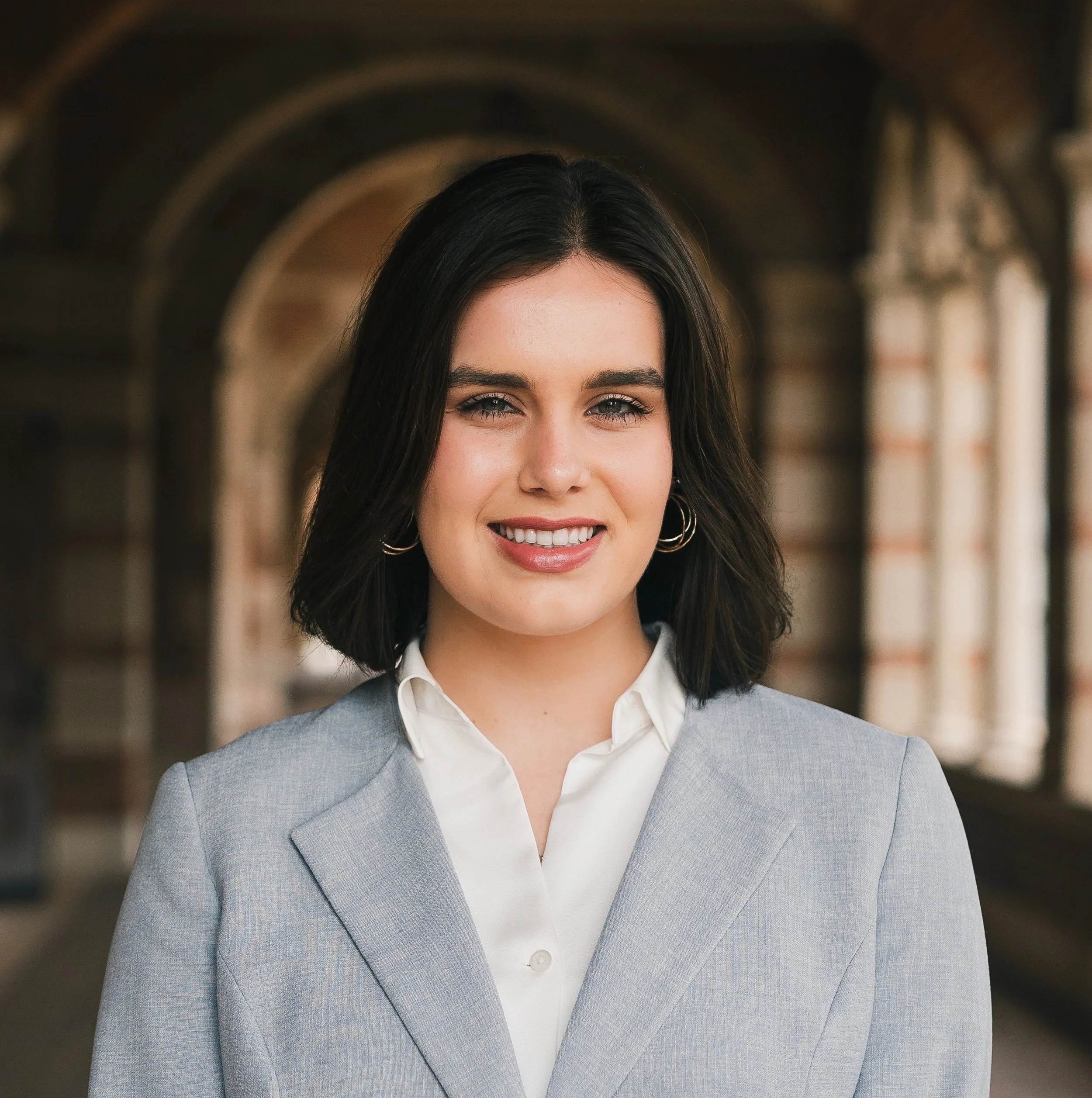 Headshot of smiling female tutor with medium-length brown hair wearing a grey suit and white shirt.