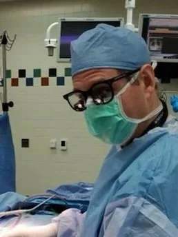 A surgeon in scrubs, cap, and mask in a hospital operating room.