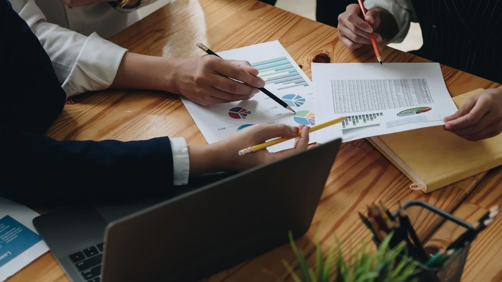 People analyzing documents with graphs and charts at a wooden table in a business meeting.