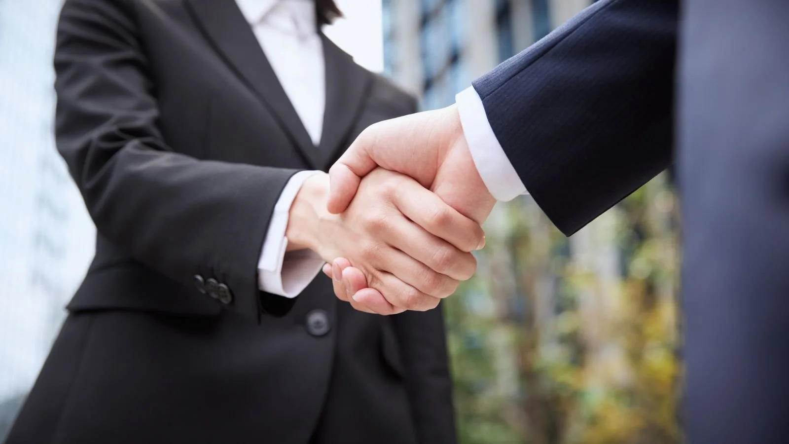 Close-up of two people in formal business suits shaking hands outdoors.
