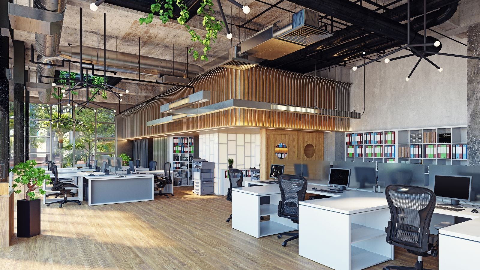 Modern open-plan office with desks, ergonomic chairs, and computers, decorated with plants and wall shelves filled with colorful binders, featuring industrial ceiling elements and natural light from large windows.
