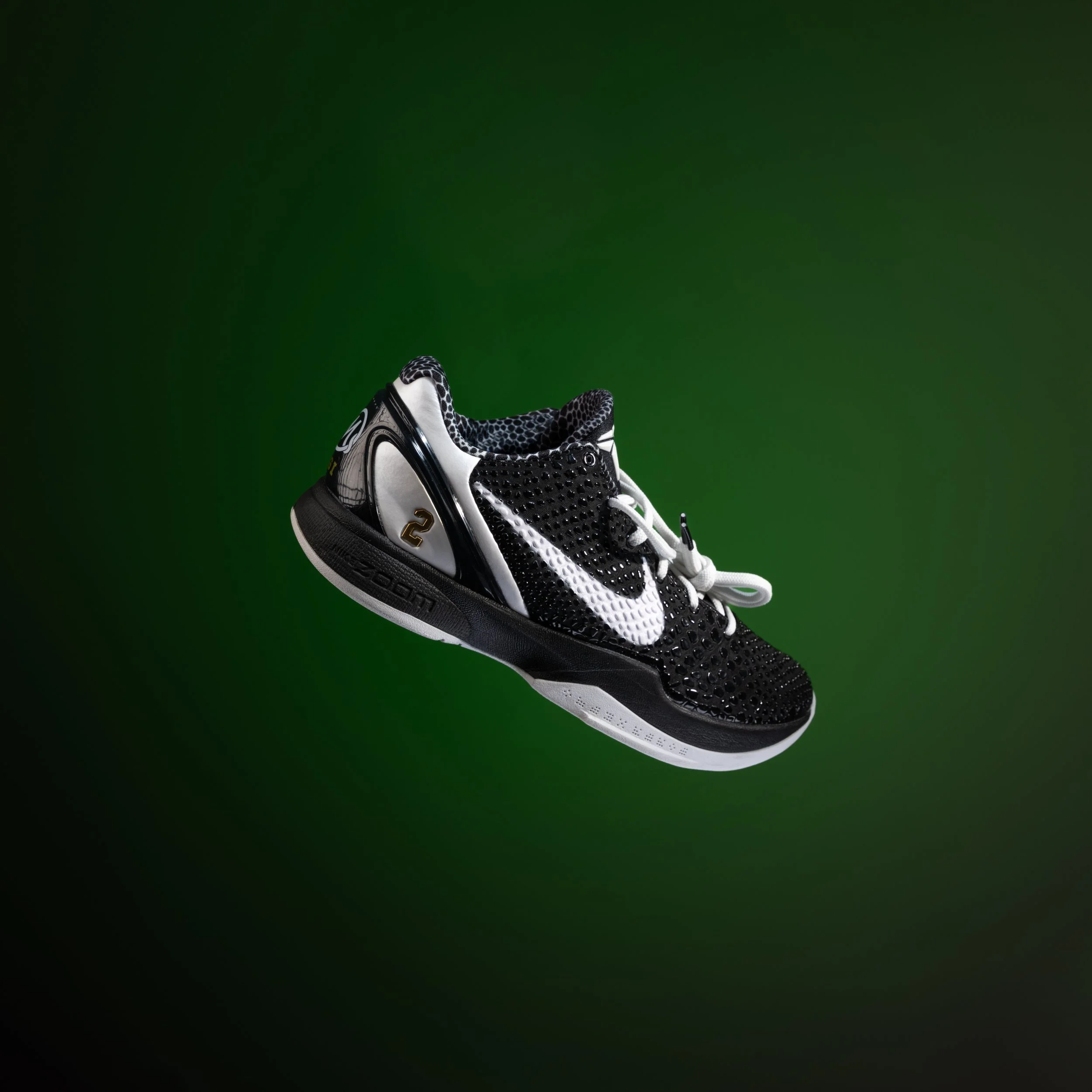 A close-up of a black and white athletic running shoe with mesh details, held against a green background.