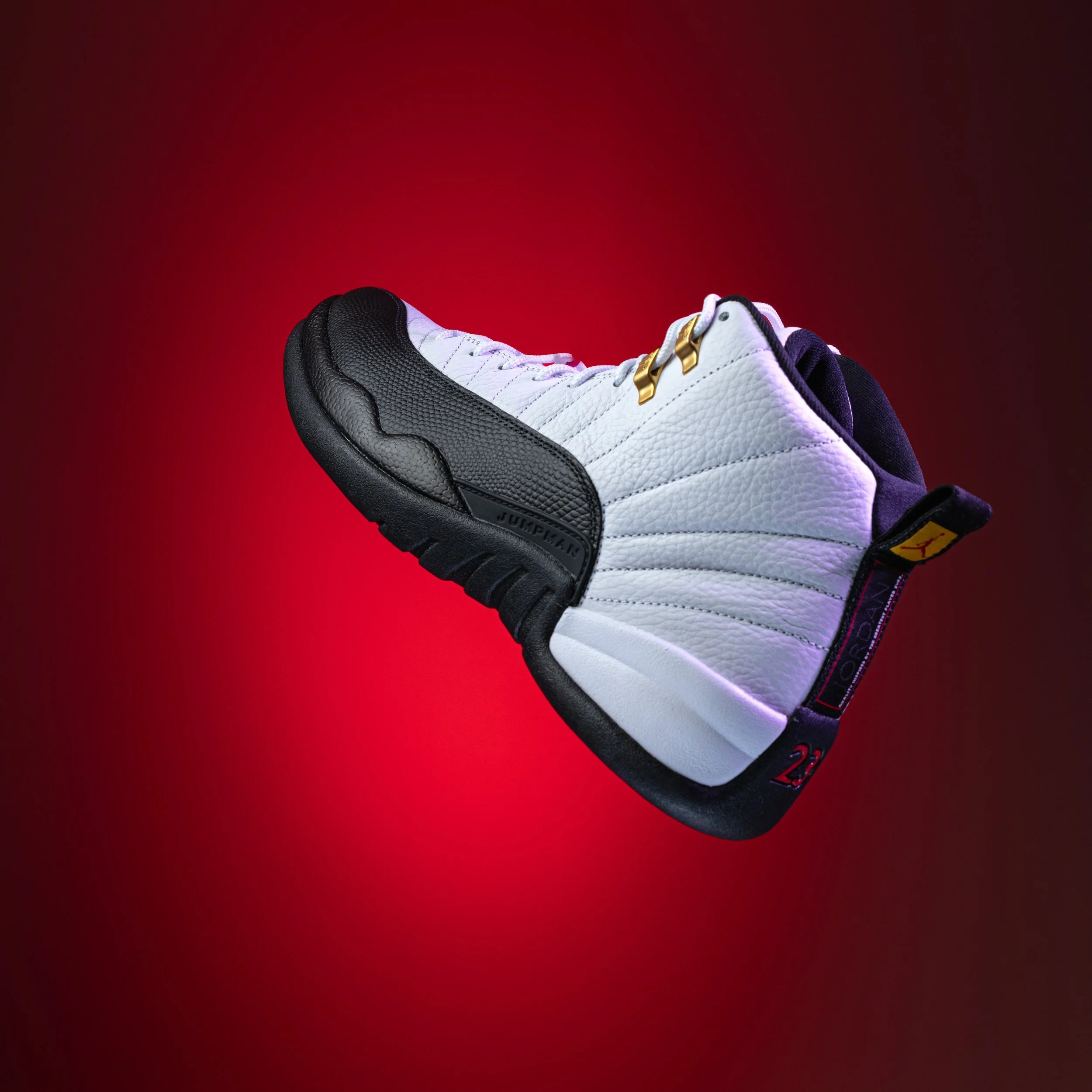 Close-up of a white sneaker with black and gold accents resting on a red background.