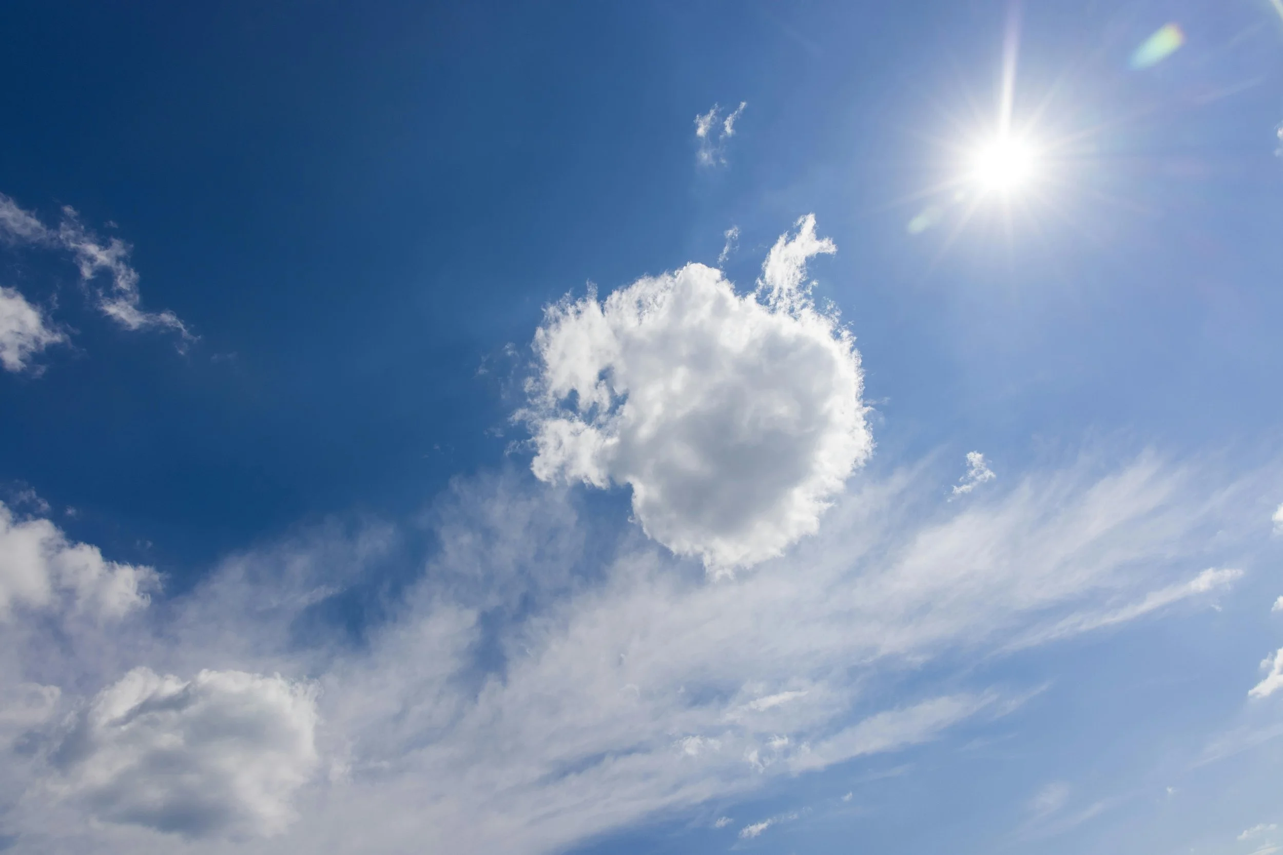 Blue sky with scattered white clouds and the sun shining brightly.