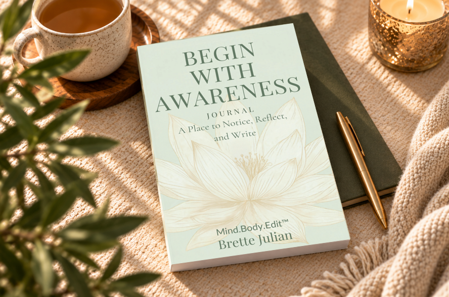 Begin With Awareness Journal with a sage green lotus cover beside a cup of tea, candle, gold pen, and cream knit blanket.