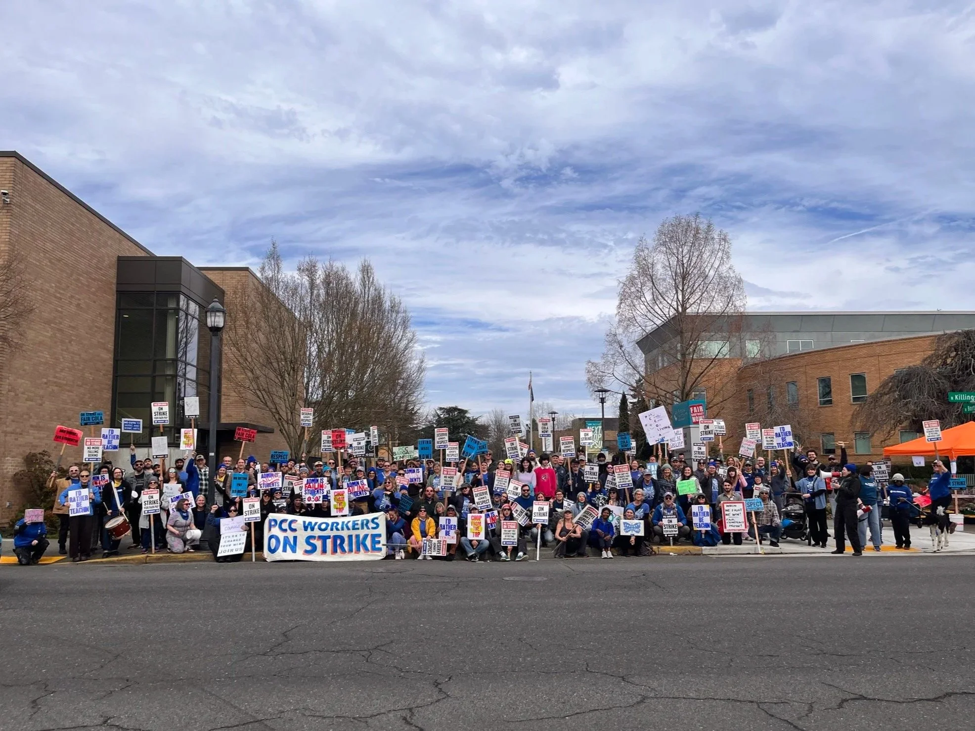 Group photo of striking workers at Cascade Campus's picket line. Folks in front are holding a big sign that reads "PCC Workers on Strike." Aenghus is in the bottom right hand corner using a megaphone.