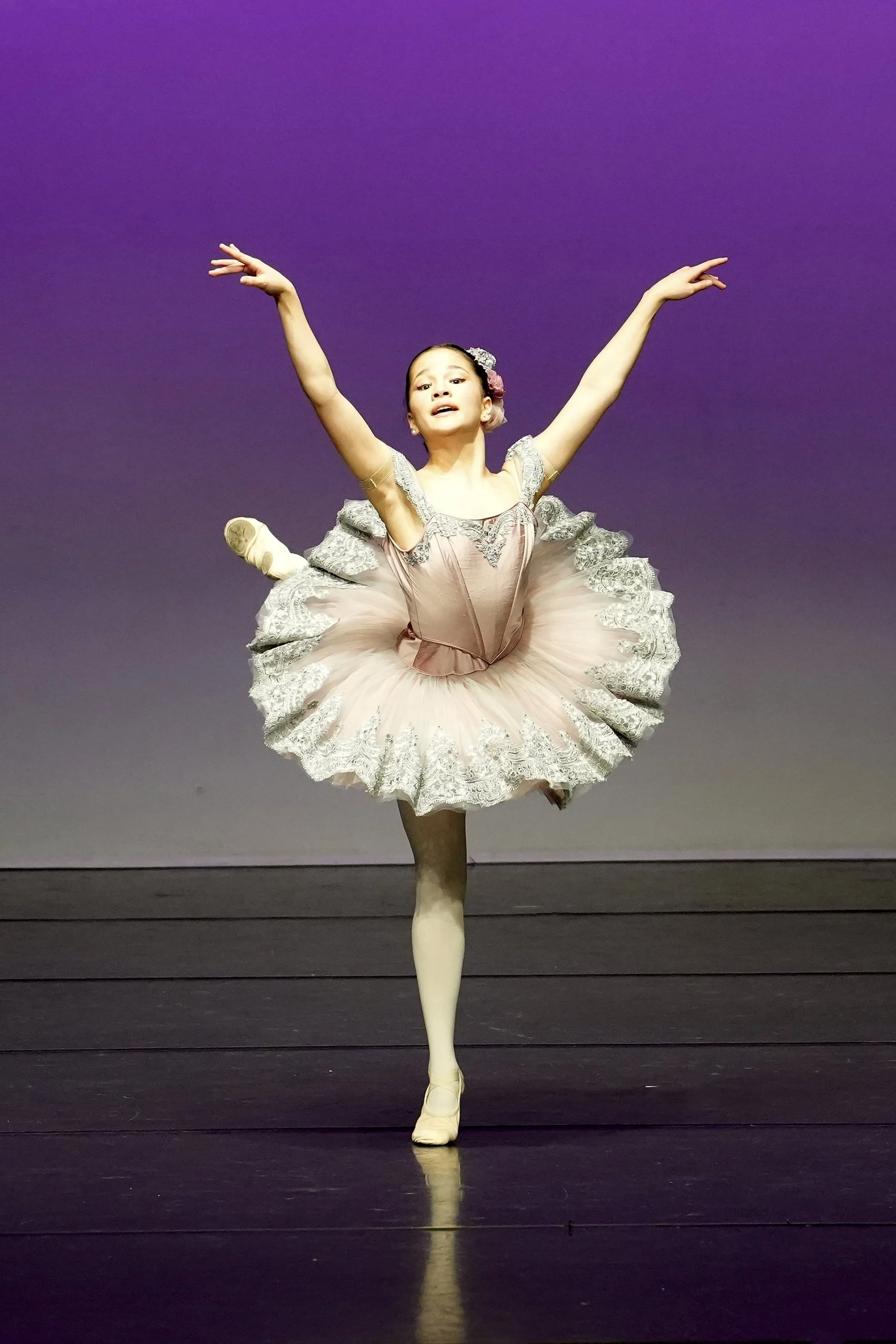 A young ballet dancer in a tutu performs on stage with a purple background.