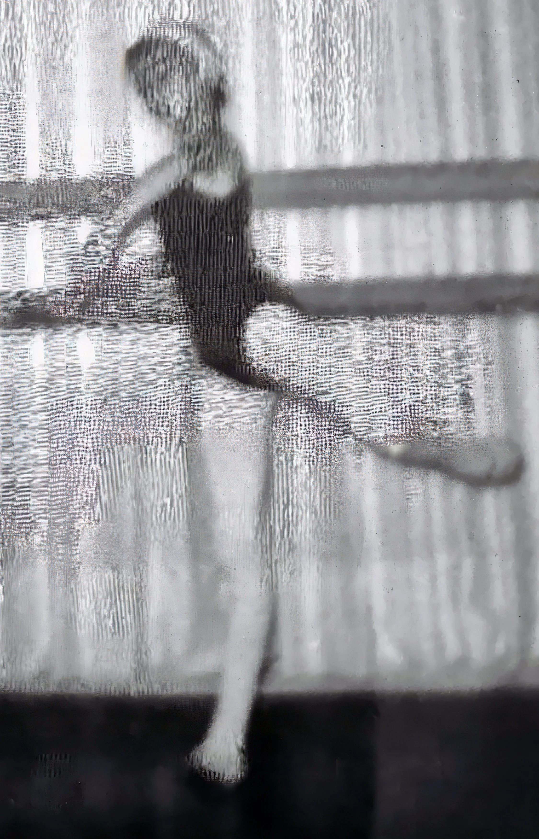 A blurry, black and white photo of a ballerina practicing dance moves in front of a curtain.