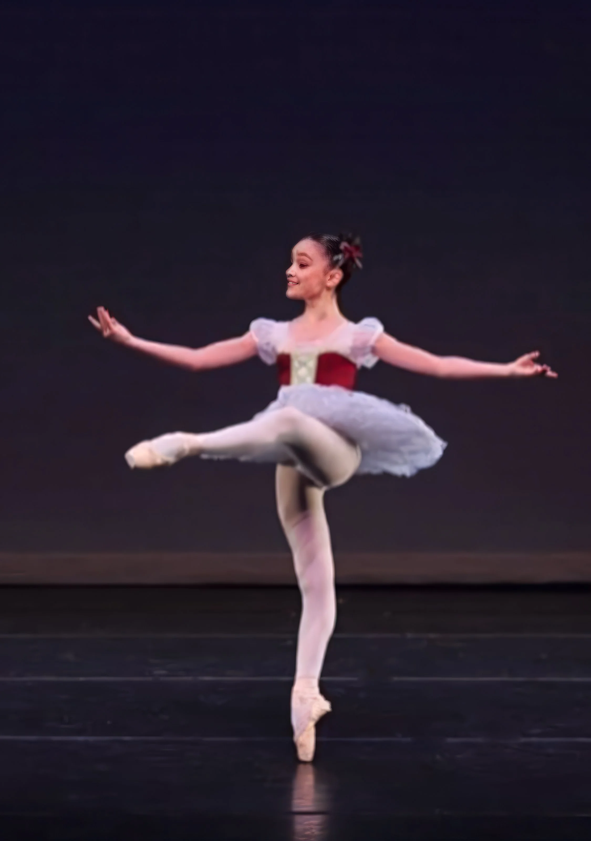 Ballet dancer performing a pose on stage, balancing on one leg with arms extended.
