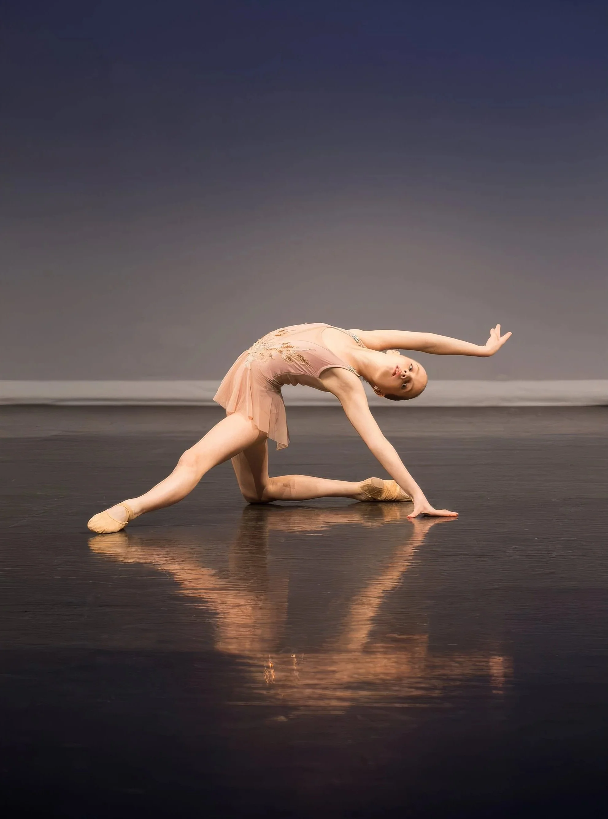 A ballet dancer performing a pose on stage with a dark background and reflective floor.