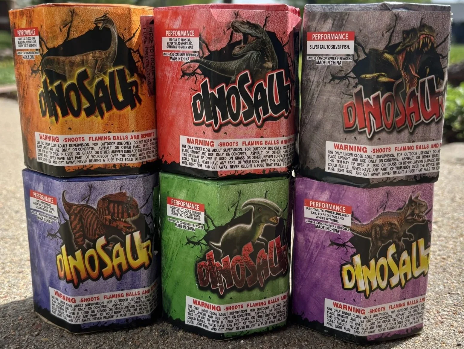 Stacked colorful fireworks boxes labeled 'Dinosaur' with illustrations of dinosaurs on each box.