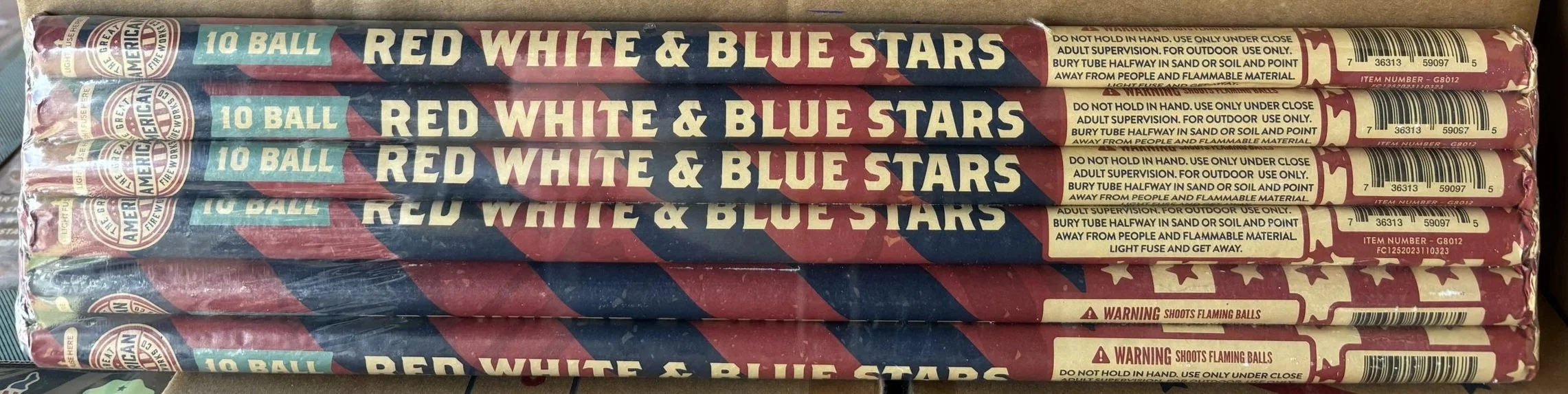 Stack of five cylindrical fireworks packages labeled '10 Ball Red White & Blue Stars' with warning labels and barcodes.