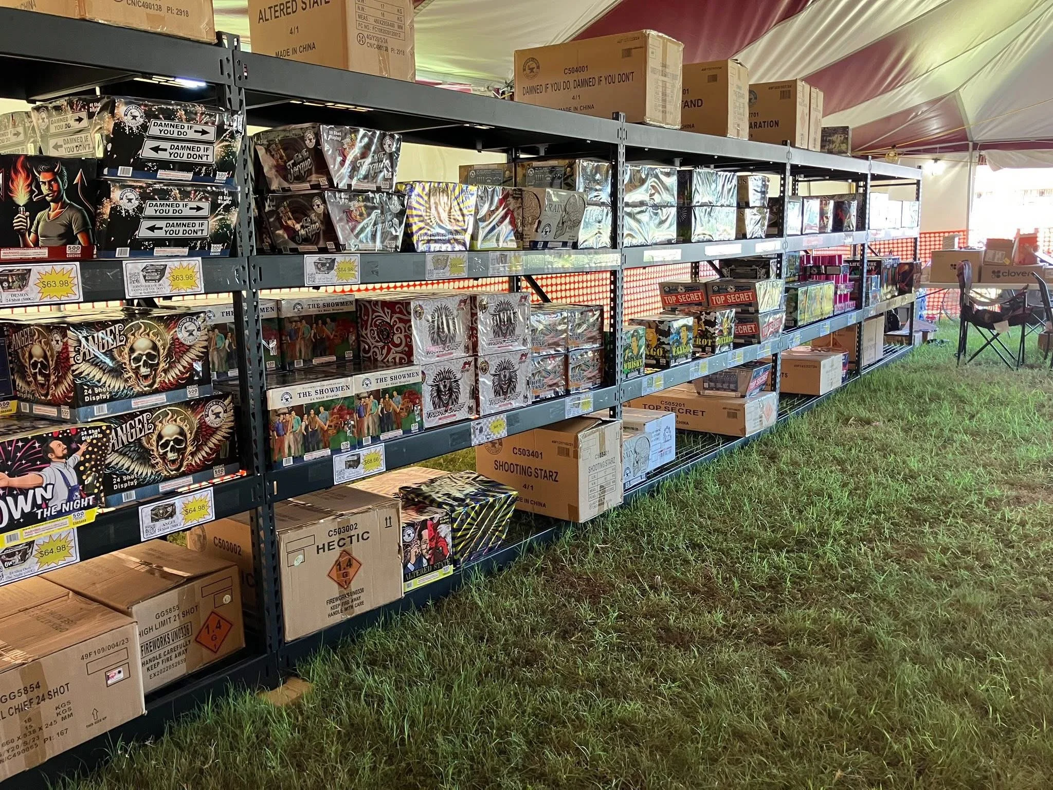 Shelves filled with boxes and fireworks inside a tent at an outdoor event.
