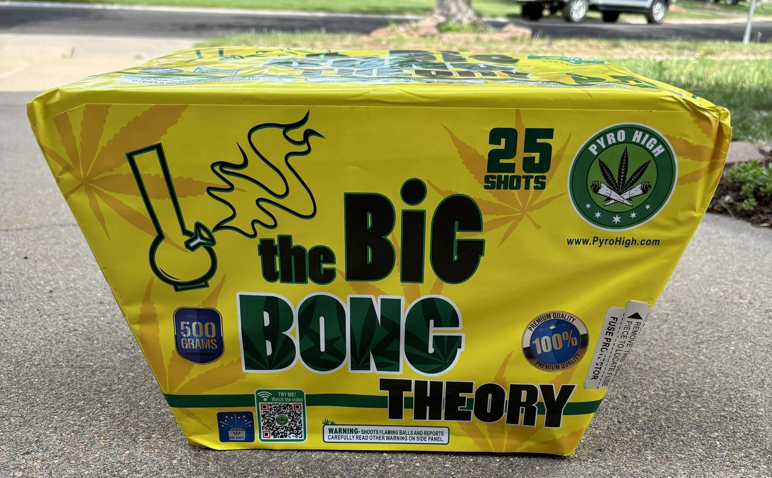 Yellow box of fireworks labeled 'Big Bang Theory' with cannabis leaf design, indicating 25 shots, 500 grams, and a warning about flaming balls and reports.