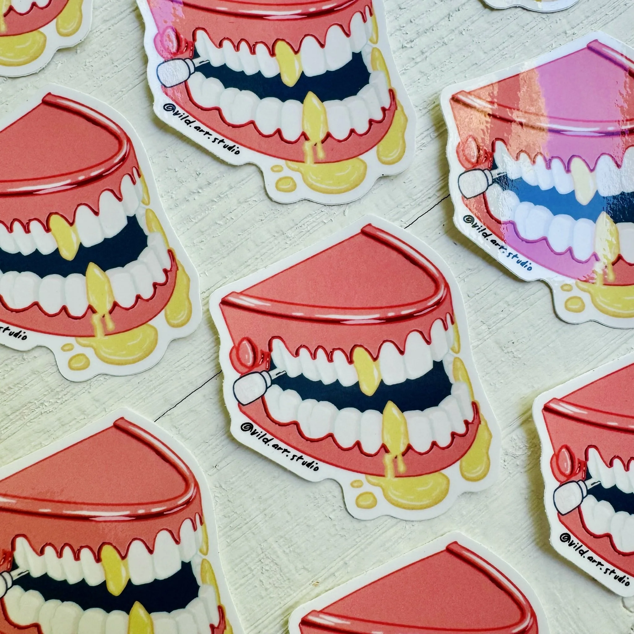Colorful stickers of open mouths with teeth, some with yellow stains, and a microphone, arranged on a white wooden surface.