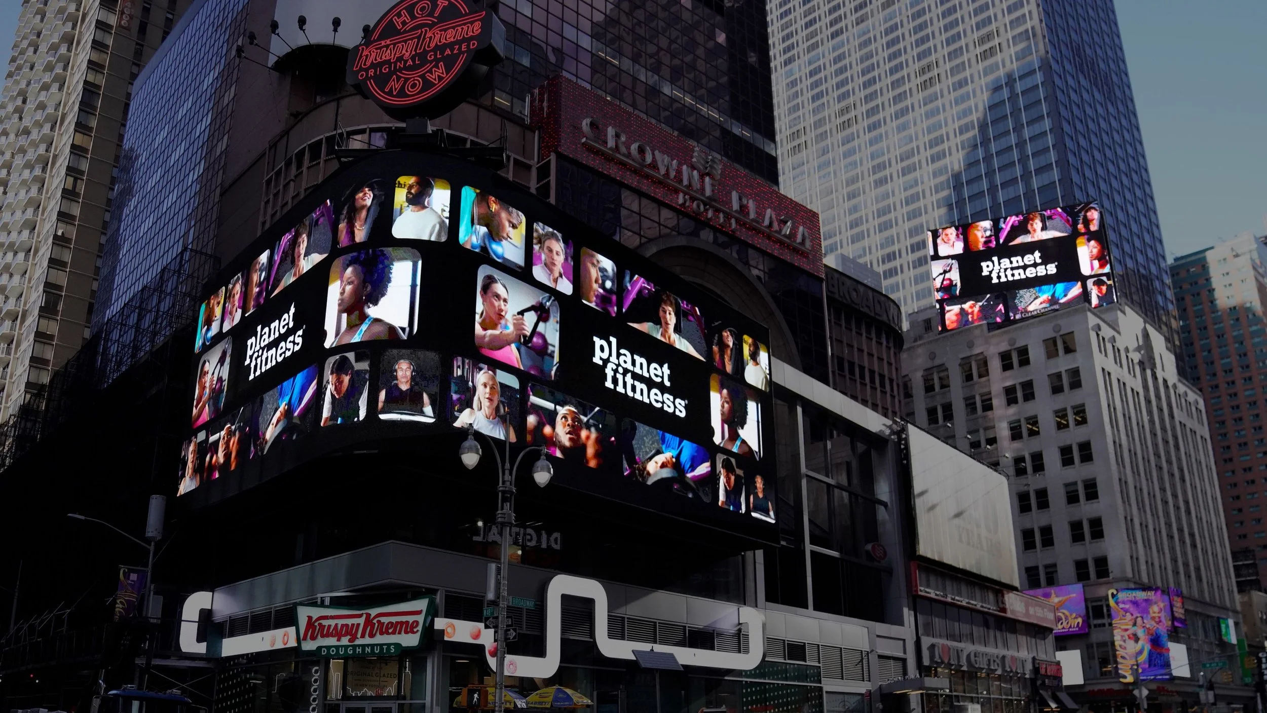 Large digital billboard in Times Square showing advertisements for Planet Fitness, specifically the We're All Strong on this Planet campaign. 